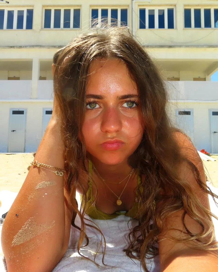 Ariana, founder of Maré, wearing gold jewellery by the beach
